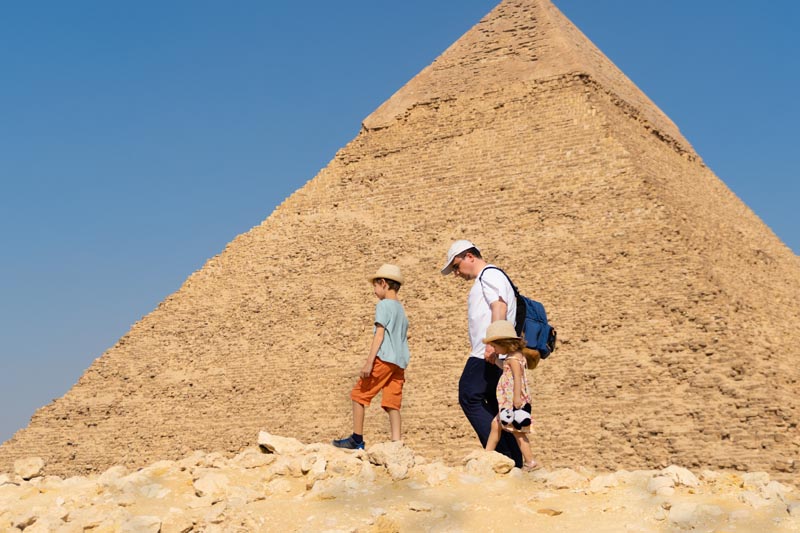 Visite en famille des pyramides de Gizeh en Égypte © Igor/stock.adobe.com Un père et ses deux enfants devant la pyramide de Khéphren à Gizeh en Égypte