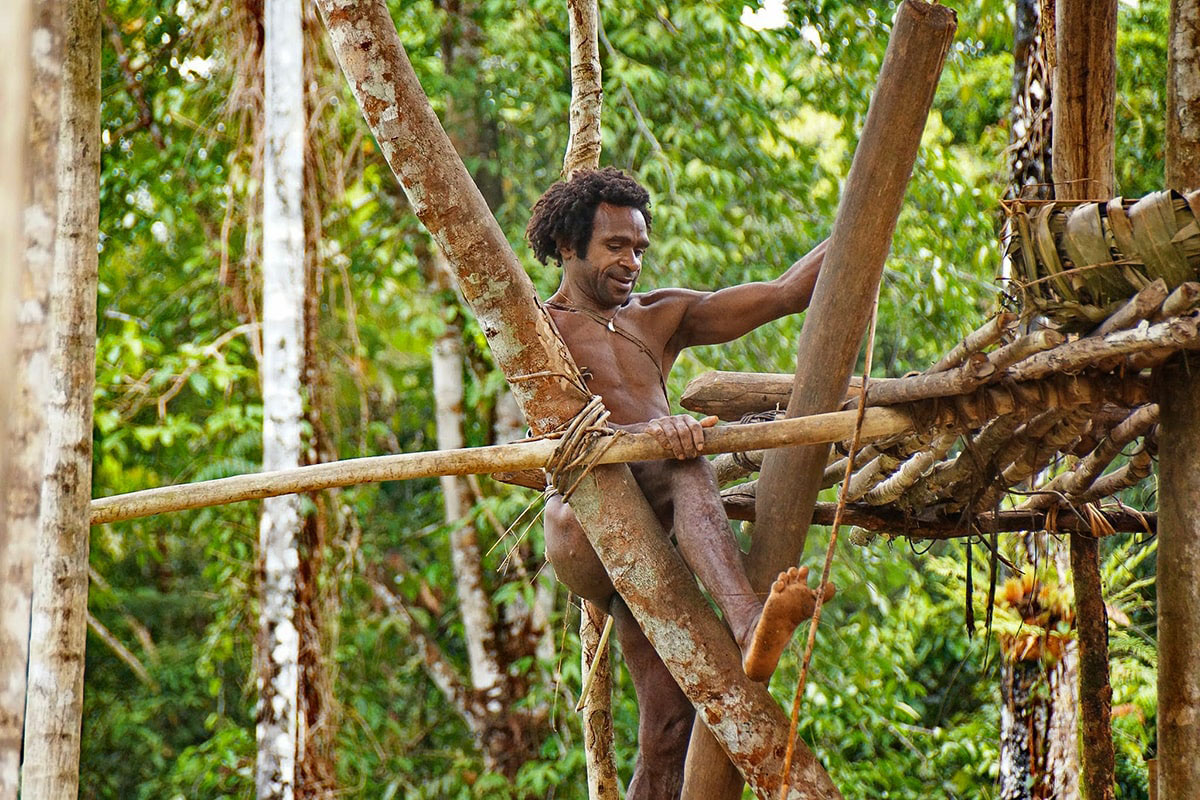 Homme Korowaï en train de construire sa maison en Papouasie